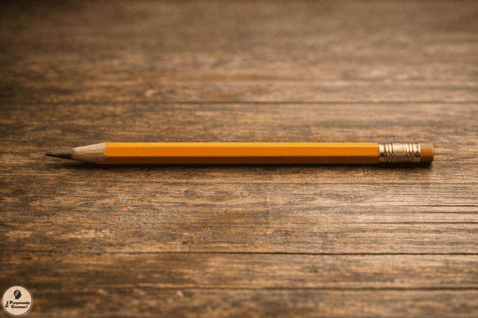 Illustration of a finished yellow pencil resting on a wooden surface, with its sharpened point, ferrule, and eraser clearly visible.